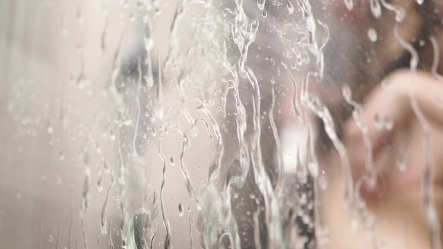 Woman Washing In Shower. Girl Showering And Washing Herself. defocusing view trough the glass with droplets 