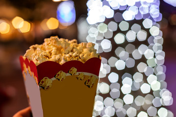 Paper cup with popcorn at night on lights background, close up