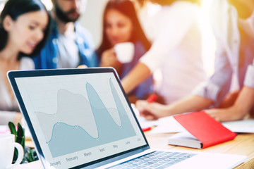 Modern laptop with diagram or graph on screen stands on table on business start up team background