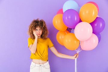 Fototapeta na wymiar Image of frustrated unhappy curly woman frowning while standing with multicolored air balloons