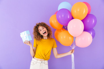 Image of beautiful young woman celebrating birthday with multicolored air balloons and present box