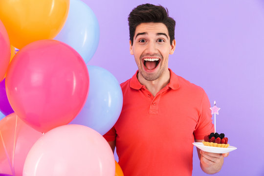 Image of optimistic joyful man celebrating birthday with multicolored air balloons and piece of pie
