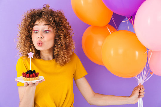 Image of happy caucasian woman celebrating birthday with multicolored air balloons and piece of pie