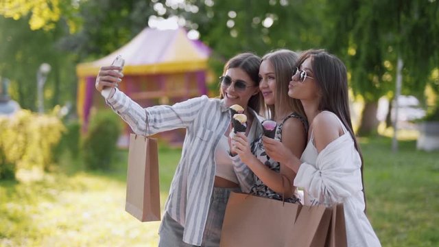 Three girlfriends together eating ice cream cones and taking selfies