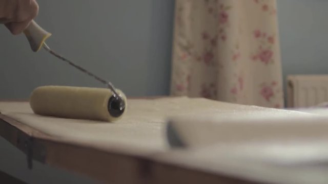 Man decorator using roller to apply adhesive paste on roll of wallpaper