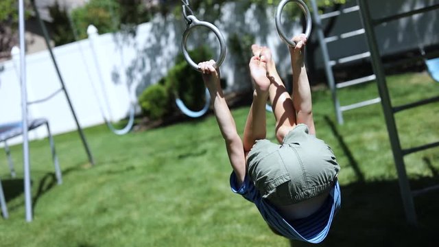 Slow Motion shot of a young boy playing on the monkey bars on a playground set in his backyard.