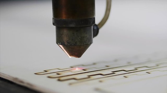 Industrial laser is cutting a pattern on a plywood sheet and moving slowly, close up.