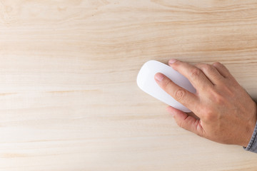 top view of a male hand with a white computer mouse on an empty wooden table