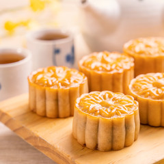 Moon cakes with tea on bright wooden table and serving try, holiday concept of Mid-Autumn festival traditional food layout design, close up, copy space.