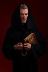 Medieval monk in black cassock with books and rosary
