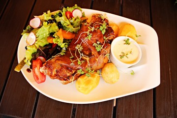Roasted pork foreshank, boiled potatoes and fresh salad on a white plate