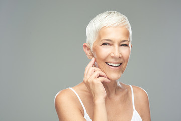 Beautiful smiling senior woman with short gray hair posing in front of gray background. Beauty photography.