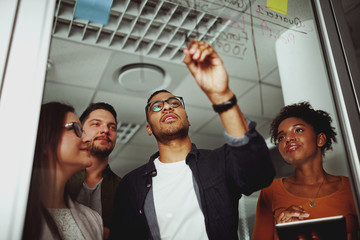Portrait of a young businessman writing on a glass board explaining his concept to his colleague