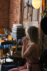 beautiful pensive calm relaxed girl blonde sits at a table in a retro vintage style cafe with a mug of drink and looks into the distance