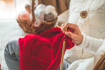 Beautiful girl knits a warm sweater on the bed. Knitting as a hobby. Accessories for knitting.