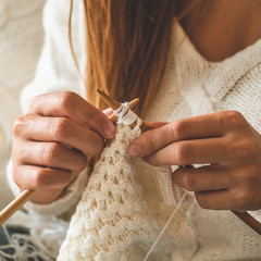 Beautiful girl knits a warm sweater on the bed. Knitting as a hobby. Accessories for knitting.