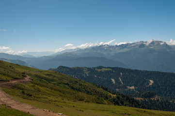 on alpine meadows of a mountain range at an altitude of more than 2 thousand meters - a view of the mountain peaks, sky and clouds of the ski resort on a sunny summer day in the Caucasus mountains