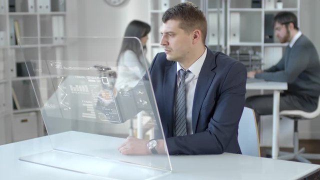 Businessman with bionic prosthetic hand sitting at desk in the office, tapping and swiping on augmented reality computer screen while working with financial data