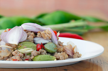 Stir fried Bitter bean (sato) with shrimp paste and minced pork (thai southern food) in white dish on brown wooden table