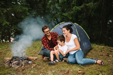 Family near the fire in the forest. Parent with child on a tent background. National Park. Hike with children. Active summer holidays.