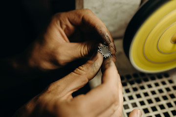 Crafting. Hands of the jeweler polishes silver jewelry brooch on the polishing wheel. Little gain on photo - 287567894