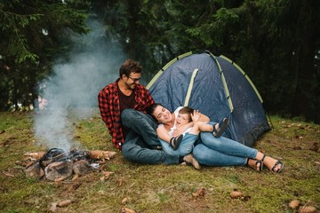 Family near the fire in the forest. Parent with child on a tent background. National Park. Hike with children. Active summer holidays.