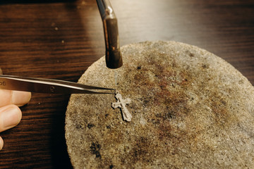 Crafting. Professional jeweler using gas torch for melting precious cross. Jewelry specialist...
