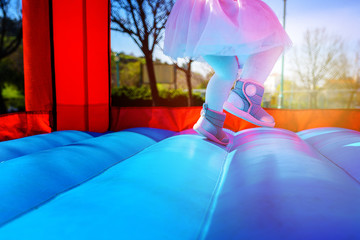 Close-up portrait of female joyful little girl legs jumps on a big inflatable trampoline outdoors in the park.