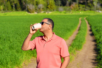 Happy elderly man in a summer field on forest background drink morning coffee from one-time cardboard cup.