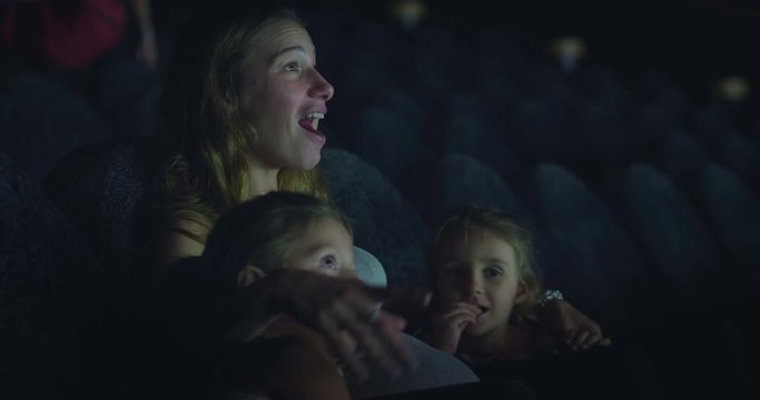 Authentic shot of an young mother with two daughters are excited to enjoy a family movie in a cinema.