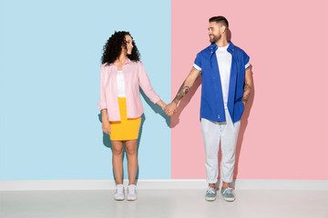 Obraz premium Young emotional caucasian couple in bright casual clothes posing on pink and blue background. Concept of human emotions, facial expession, relations, ad. Man and woman holding hands, smiling.