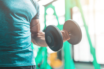 Cropped portrait of caucasian athletic man holding dumbell and showing his muscular arm. Man doing...