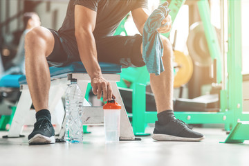 Cropped portait of athletic man sitting and taking a classic fitness shaker with pre-workout drink in it. Sports nutrition concept. Horizontal shot