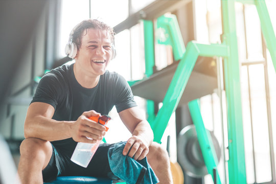 Portait of cheerful athletic man in headphones listening to music and holding a towel and a classic fitness shaker with pre-workout drink in it. Sports nutrition concept. Horizontal shot
