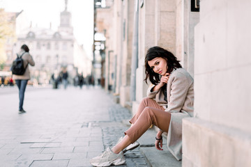 Outdoor portrait of a young beautiful fashionable lady sitting on stairs of old building on a...