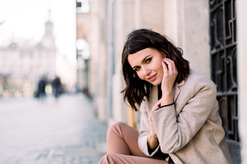Street portrait of young beautiful happy smiling woman wearing stylish coat and pants. Model looking at camera. Female fashion concept. Copy space, free text
