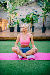 Young athletic woman sitting on yoga mat in yard on summer day