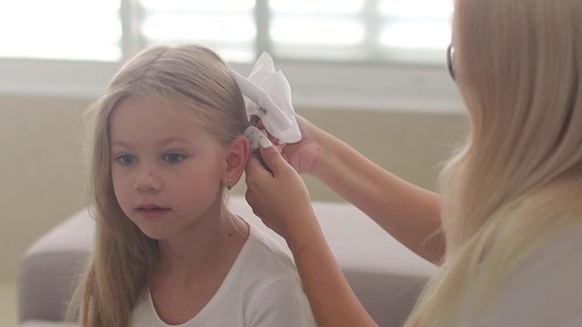 Mother enjoying time with her daughter at home. A young woman is sitting on the couch and combing her daughter in the morning after waking up and mom is doing her hairstyle with white bows in slowmo