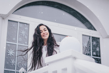 Happy woman with long hair in white sweater standing under snowfall.