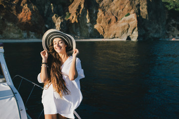 Happy woman in hat and beach clothes posing on a yacht.
