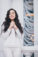 Happy woman with long hair in white sweater standing under snowfall.
