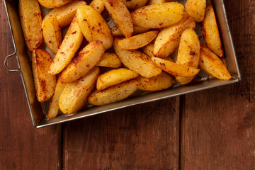 Potato wedges, oven baked, close-up overhead shot in a baking tray on a dark rustic wooden background