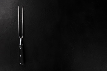 A carving fork for meat, shot from the top on a black background with a place for text