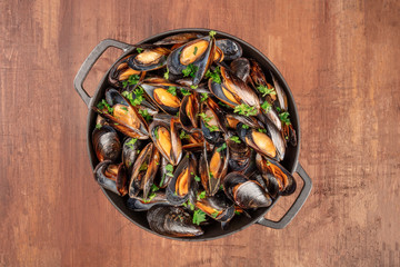 Marinara mussels, moules mariniere, cooked in a cooking pan, shot from above on a dark rustic background