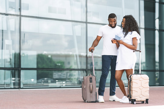 Cheerful african millennials reading flight information, airport exterior