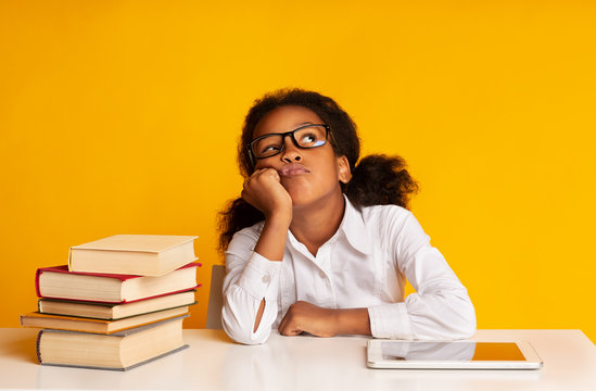 Bored Schoolgirl Sitting Between Tablet And Book Stack In Studio