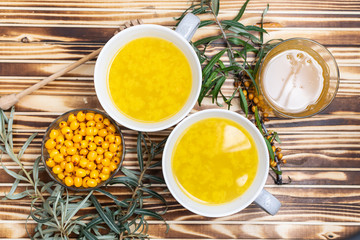 Fresh organic homemade sea buckthorn tea with green branches of sea buckthorn, berries and honey on rustic wooden table top view. Vitamin autumn drink.