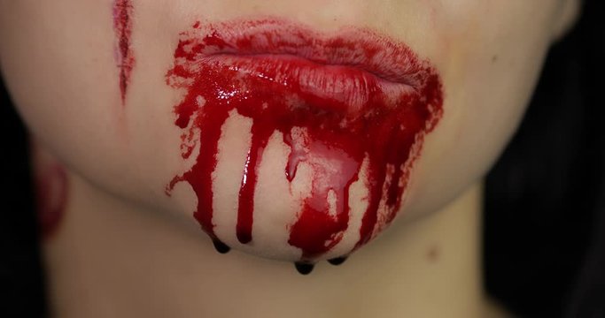 Bloody mouth and teeth of girl. Vampire Halloween makeup with dripping blood