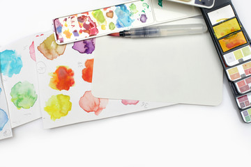 Box with watercolors, brush and palette on a light gray paper background. Flat lay.  Top view...