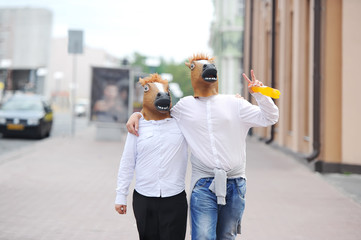 Couple wearing horse masks walking in city street.